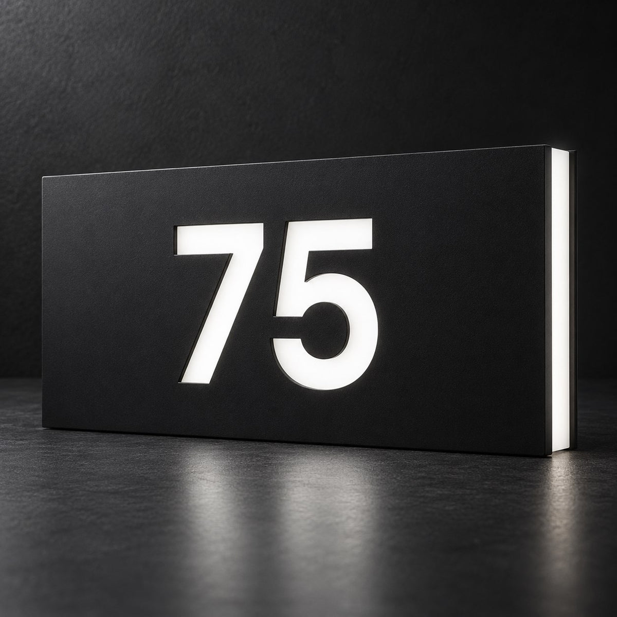 Matte black illuminated house number sign, The Kawana, displaying 75 in glowing white on a dark background.