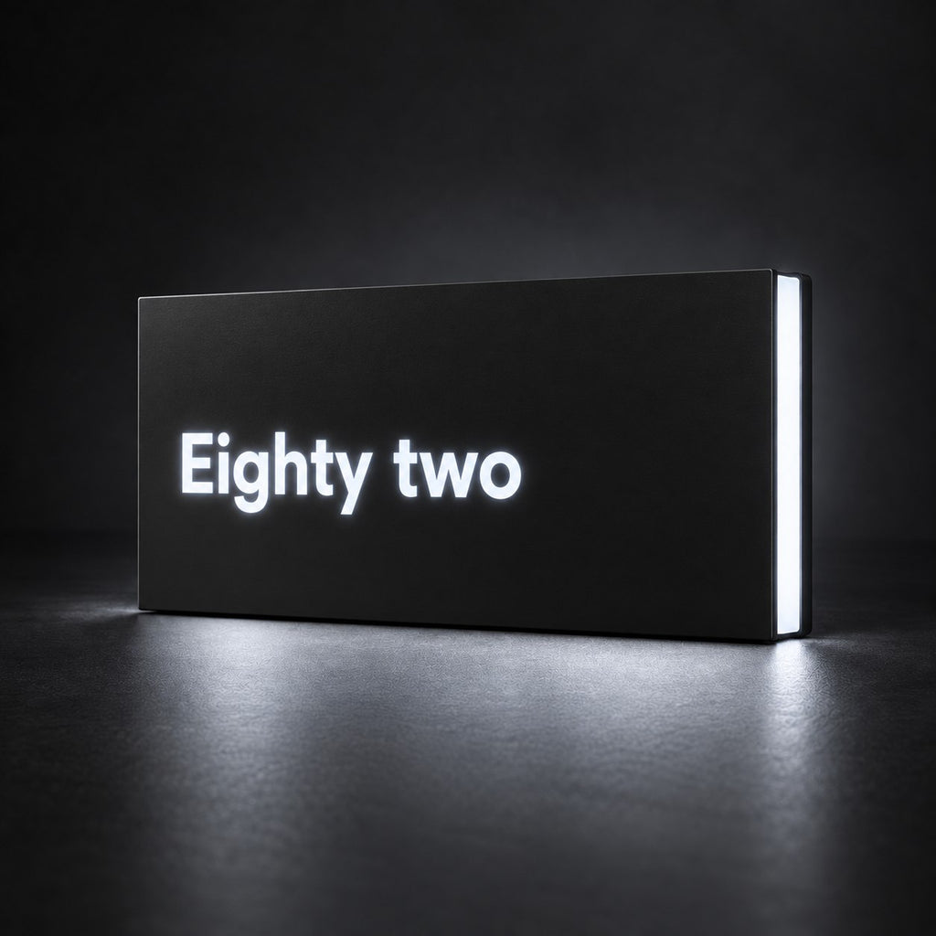 Matte black illuminated house number sign, The Montville, with the number spelled out as Eighty two, lit from behind in white.