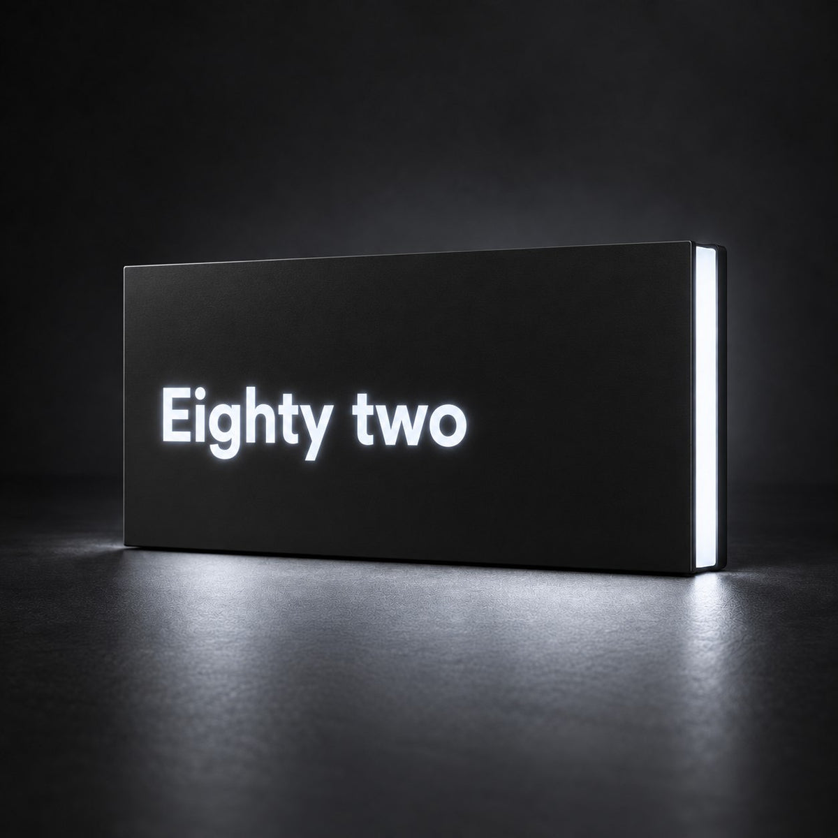 Matte black illuminated house number sign, The Montville, with the number spelled out as Eighty two, lit from behind in white.