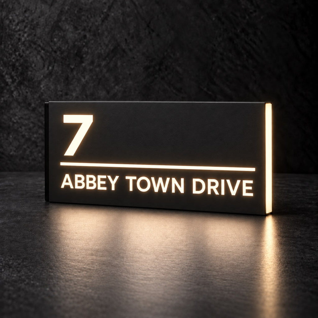 Matte black illuminated house number and street name sign, The Noosa, 7 Abbey Town Drive with the number, rule and street name cut through and lit from behind in warm white.