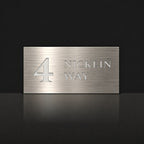 Brushed silver house number and street name sign with a brushed metal look, The Marcoola, reading 4 Nicklin Way in white lettering.