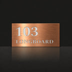 Brushed copper house number and street name sign with a brushed metal look, The Peregian, reading 103 Longboard in white lettering.