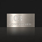 Brushed silver house number and street name sign with a brushed metal look, The Peregian, reading 103 Longboard in white lettering.