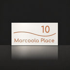 Brushed copper house number and street name sign with a brushed metal look, The Bokarina, white face reading 10 Marcoola Place in copper lettering, with a wave line.