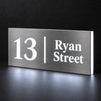 Brushed silver illuminated house number and street name sign with a brushed metal look, The Coolum, 13 Ryan Street with the number, rule and street name lit from behind in cool white.