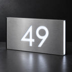 Brushed silver illuminated house number sign with a brushed metal look, The Kawana, showing the number 49 in bright white LED cutouts on a dark background.