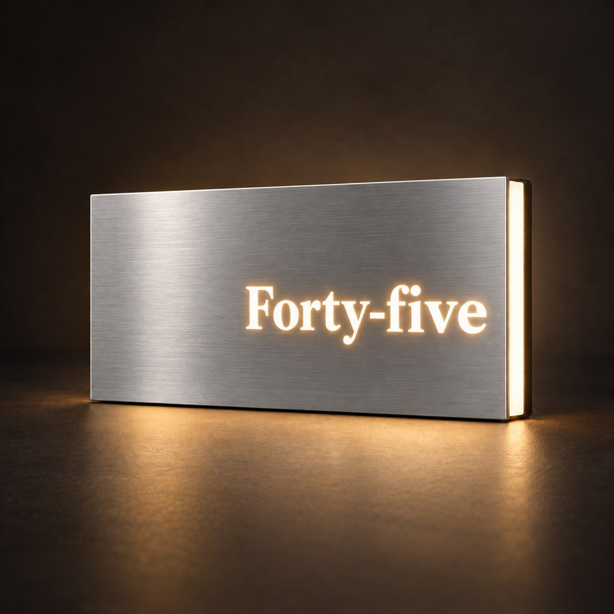 Brushed silver illuminated house number sign with a brushed metal look, The Montville, with the number spelled out as Forty-five, lit from behind in warm white.