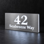 Brushed silver illuminated house number and street name sign with a brushed metal look, The Peregian, 42 Seabreeze Way cut through and lit from behind in cool white.
