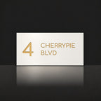 Brushed gold house number and street name sign with a brushed metal look, The Maleny, white face reading 4 Cherrypie Blvd in gold lettering.