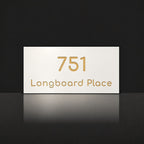 Brushed gold house number and street name sign with a brushed metal look, The Peregian, white face reading 751 Longboard Place in gold lettering.