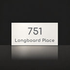 Matte white house number and street name sign, The Peregian, reading 751 Longboard Place in charcoal lettering.