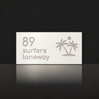 Brushed silver house number and street name sign with a brushed metal look, The Yaroomba, white face reading 89 Surfers Laneway in silver lettering, with palm trees and a sun.