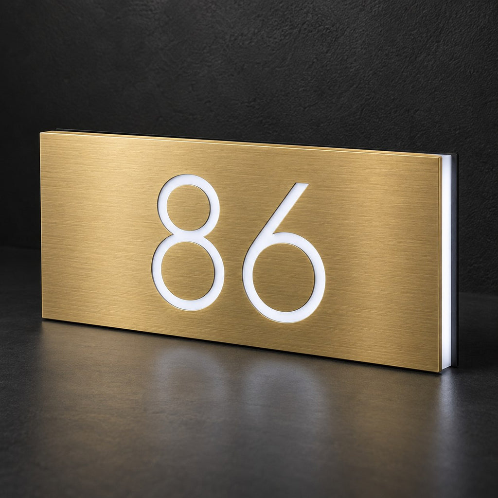 Brushed gold illuminated house number sign with a brushed metal look, The Kawana, displaying 86 in a glowing white LED cutout against a dark background.
