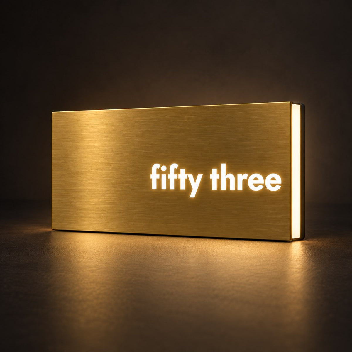 Brushed gold illuminated house number sign with a brushed metal look, The Montville, with the number spelled out as fifty three, lit from behind in warm white.