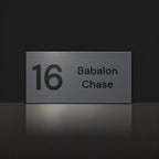 Matte charcoal house number and street name sign, The Marcoola, reading 16 Babalon Chase in black lettering.