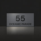 Matte charcoal house number and street name sign, The Peregian, reading 55 Oceanic Parade in black lettering.
