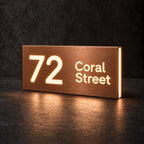 Brushed copper illuminated house number and street name sign with a brushed metal look, The Marcoola, 72 Coral Street cut through and lit from behind in warm white.