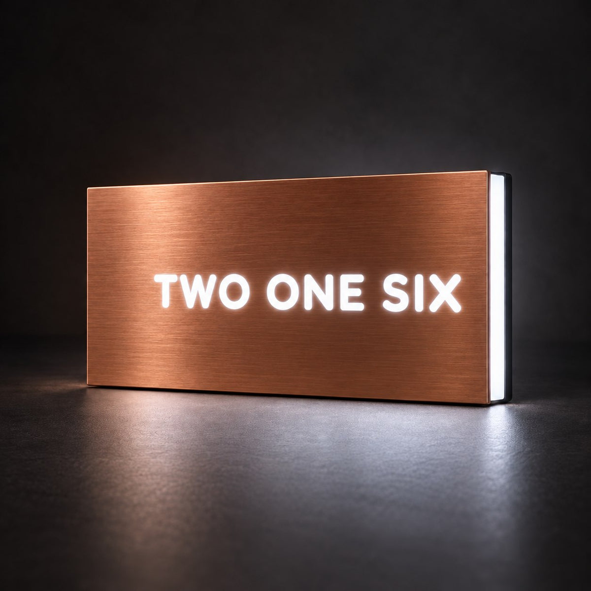 Brushed copper illuminated house number sign with a brushed metal look, The Montville, with the number spelled out as TWO ONE SIX, lit from behind in white.