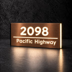 Brushed copper illuminated house number and street name sign with a brushed metal look, The Noosa, 2098 Pacific Highway with the number, rule and street name lit from behind in warm white.