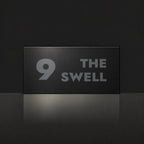Matte black house number and street name sign, The Marcoola, reading 9 The Swell in charcoal lettering.