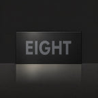 Matte black house number sign, The Montville, with the number spelled out as eight in charcoal lettering.