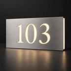 Brushed silver illuminated house number sign with a brushed metal look, The Kawana, displaying 103 lit from behind in warm white.