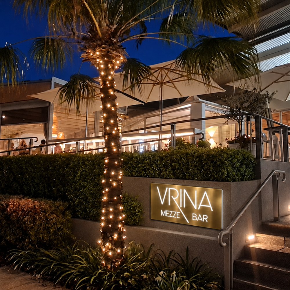 Illuminated business sign, brushed gold, on a stone plinth at the entrance to a restaurant at night
