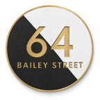Gold round house number and street name sign reading 64 Bailey Street, split diagonally into black and white with brushed gold lettering and a gold rim, The Birtinya style.