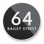 Matte round house number and street name sign reading 64 Bailey Street, split diagonally into black and charcoal with white lettering and a white rim, The Birtinya style.