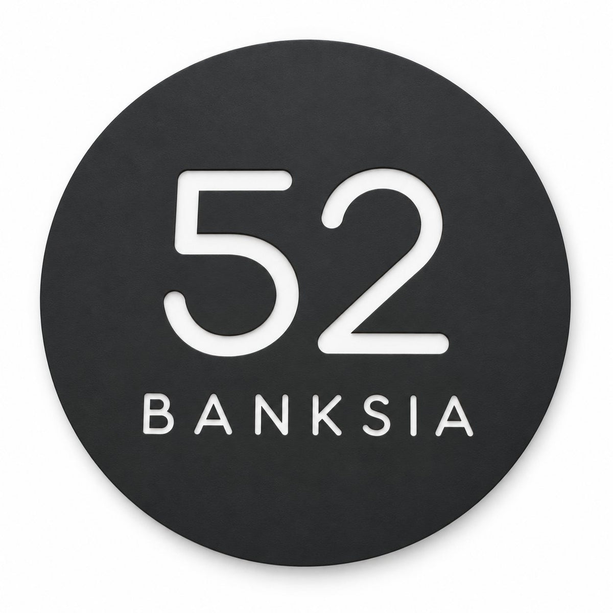 Matte black round house number and street name sign reading 52 Banksia in white, The Buderim style, on a plain white background.