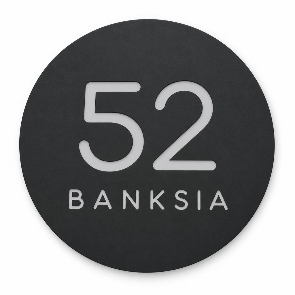 Black round house number and street name sign reading 52 Banksia in brushed silver, The Buderim style, on a plain white background.