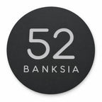 Black round house number and street name sign reading 52 Banksia in brushed silver, The Buderim style, on a plain white background.
