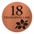 Brushed copper round house number and street name sign reading 18 Frangipani Lane with a frangipani flower cut through to black, The Currimundi style, on a plain white background.