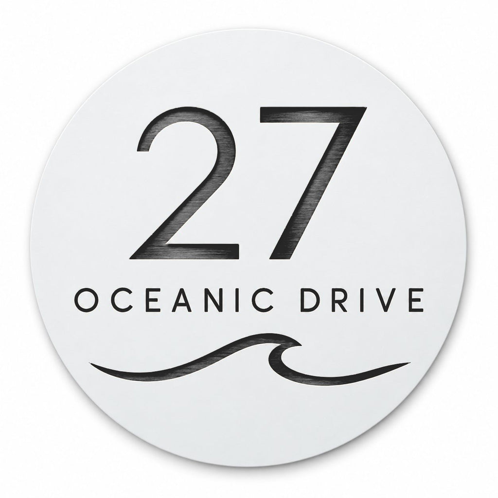 Matte white round house number and street name sign reading 27 Oceanic Drive with a curling wave, cut through to black, The Mudjimba style, on a plain white background.