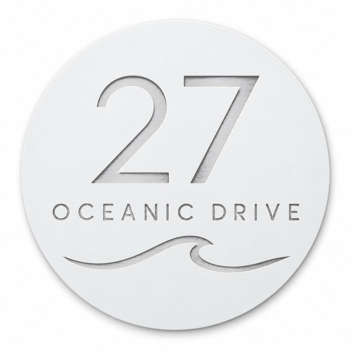 White round house number and street name sign reading 27 Oceanic Drive with a curling wave, cut through to brushed silver, The Mudjimba style, on a plain white background.